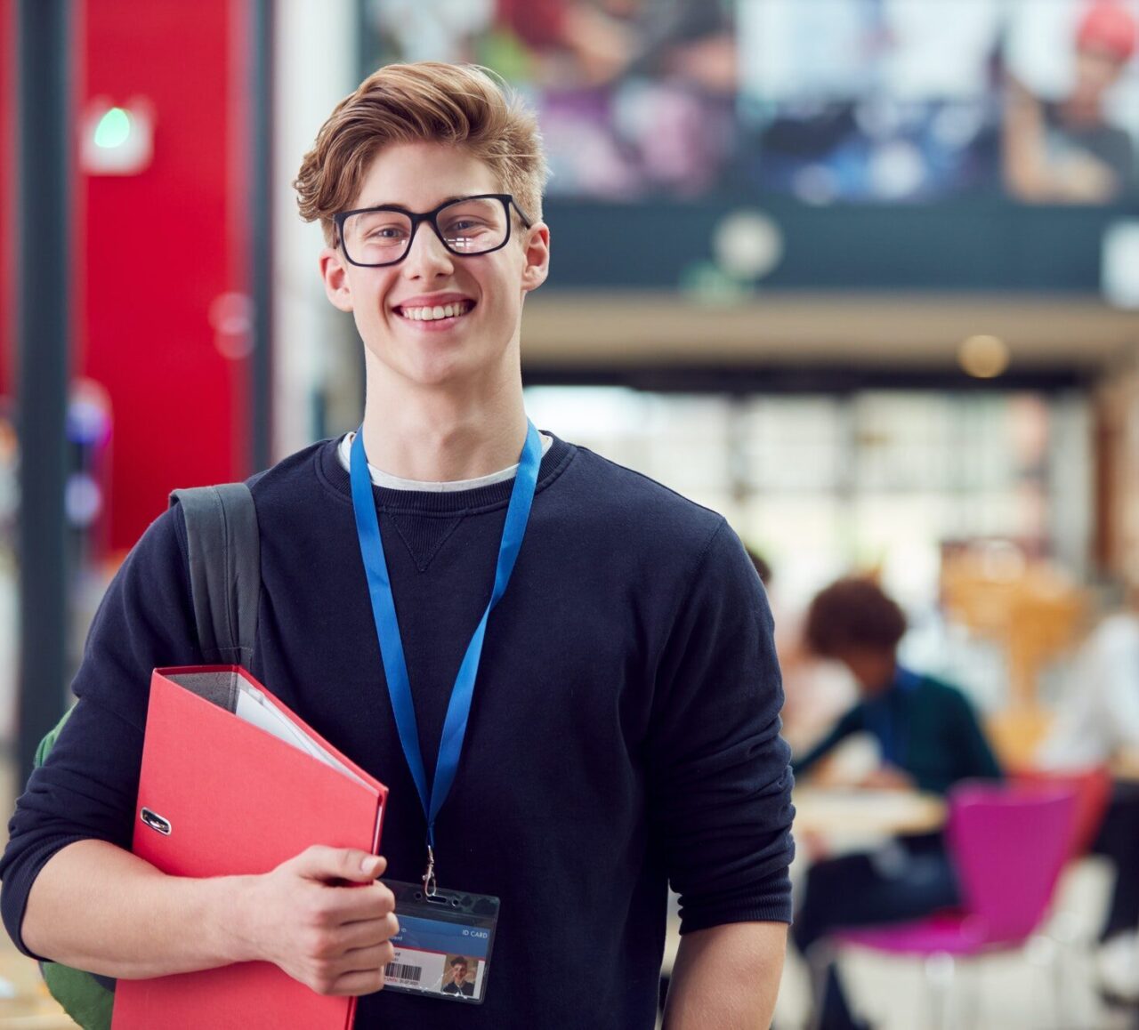 portrait-of-smiling-male-college-student-in-busy-communal-campus-building-e1701494224421